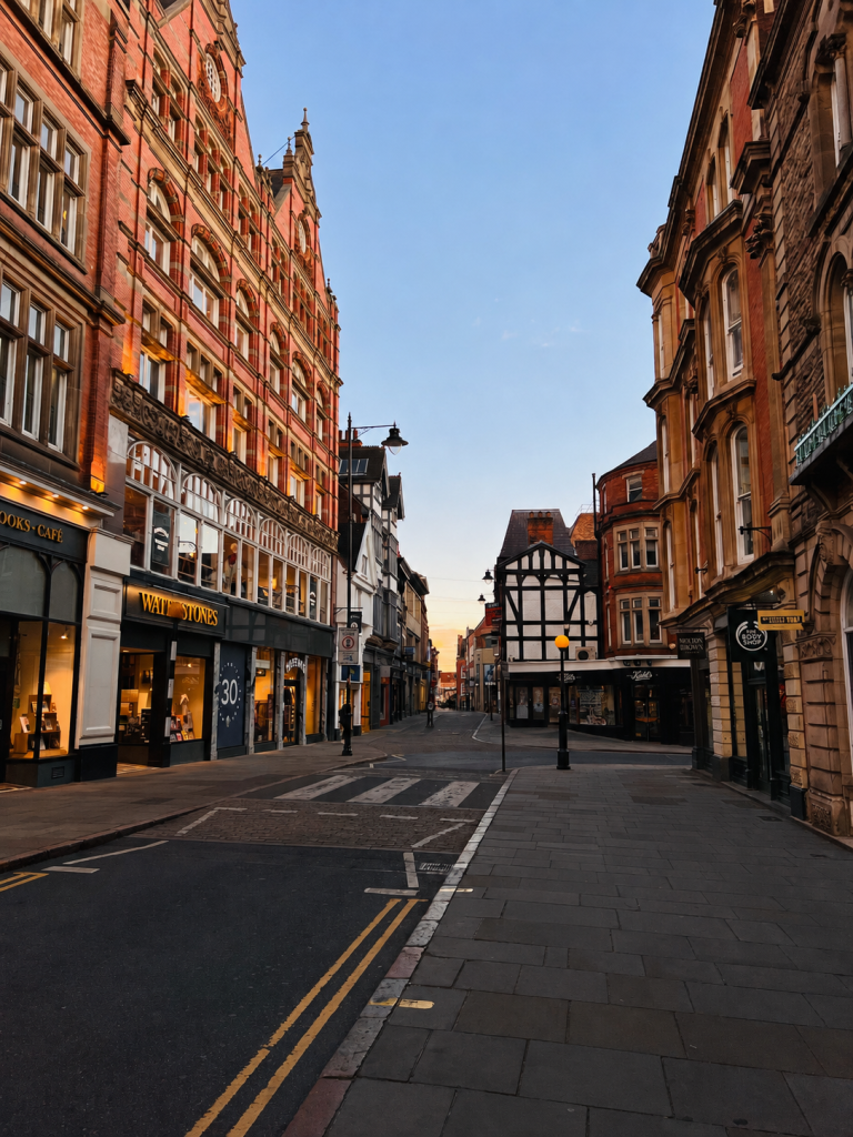 A quiet historic high street at dusk, lined with period buildings, independent shops and cafés.