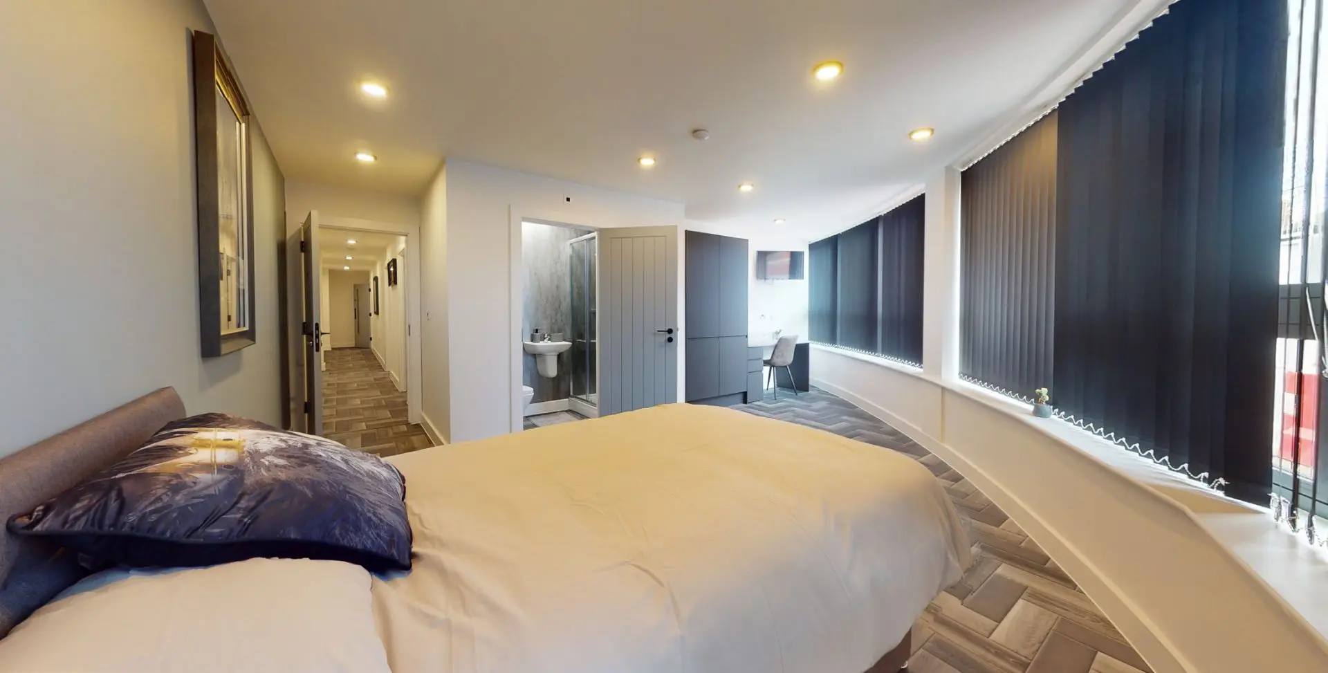 Panoramic view of a furnished student bedroom at Graduation House with double bed, floor-to-ceiling curved windows, fitted wardrobe, study desk and en-suite shower room.