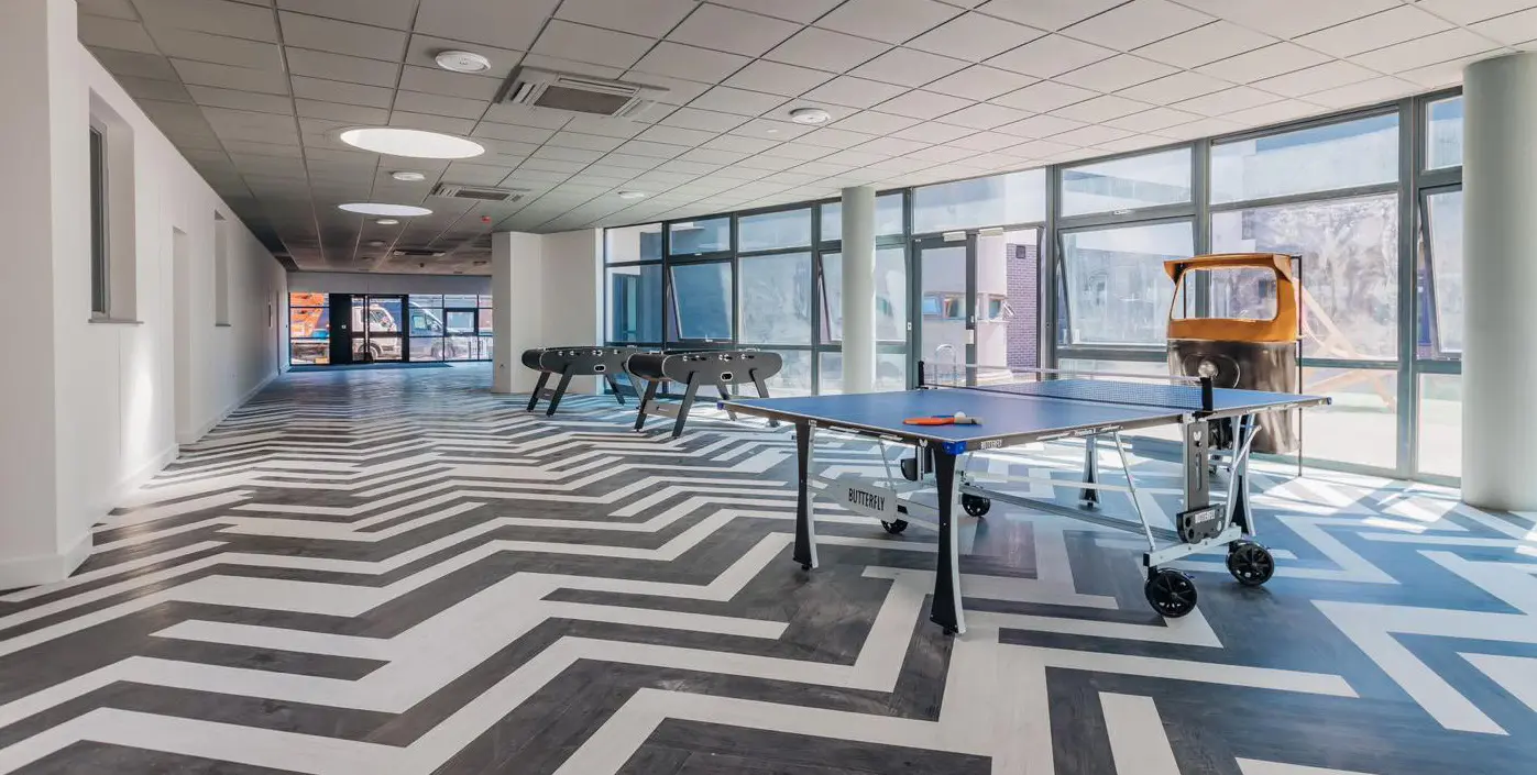 Games room at Graduation House with table tennis table, two foosball tables and floor-to-ceiling windows over a bold geometric floor.